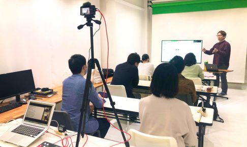白ホリスタジオでのセミナー収録とライブ配信の風景。三脚のカメラとスイッチャーを設置し、受講者と講師を撮影している