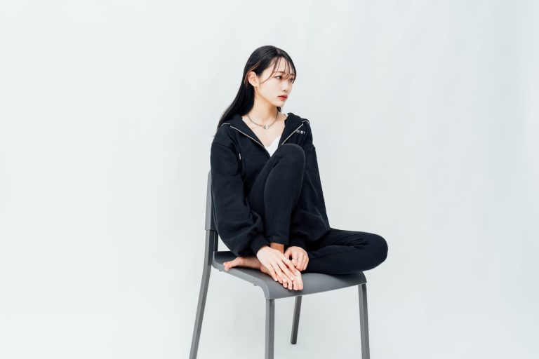 白ホリスタジオでの撮影風景。白い背景の前で椅子に座る人物を撮影したカット